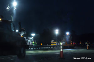 A nighttime photograph of a construction zone on an interstate highway showing several workers on foot.